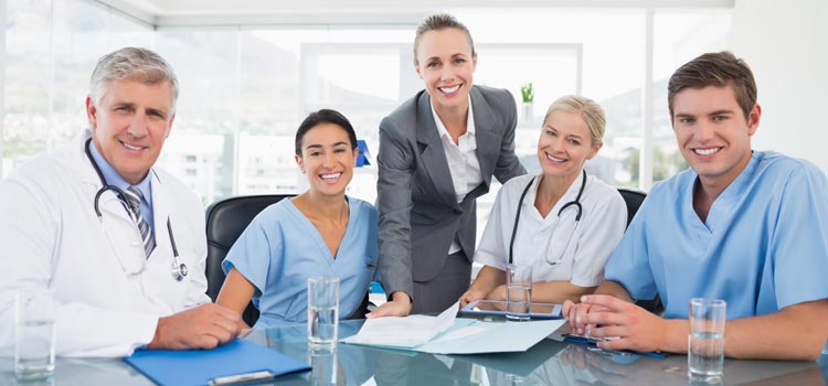 Group of nurses, doctors and executive sitting around a table, smiling for the camera