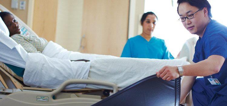 Agiliti team member places a fall mat next to a low bed in a hospital room