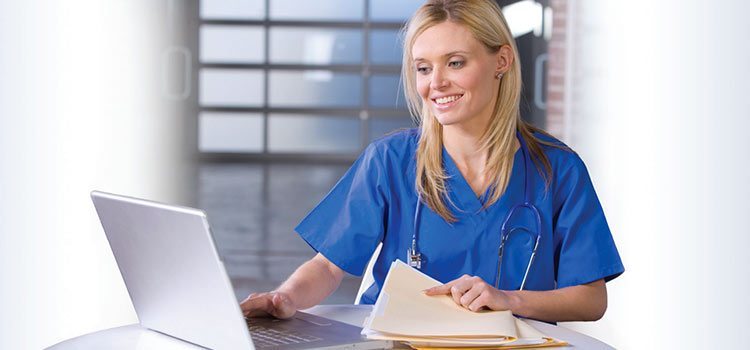 A nurse sits at a desk entering patient chart data into a computer