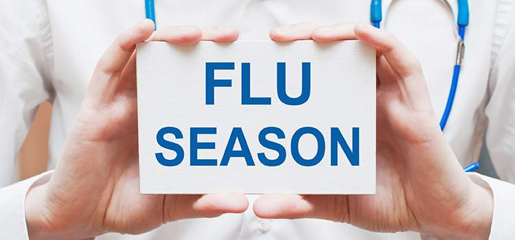 A doctor holding a sign that says, "Flu Season"