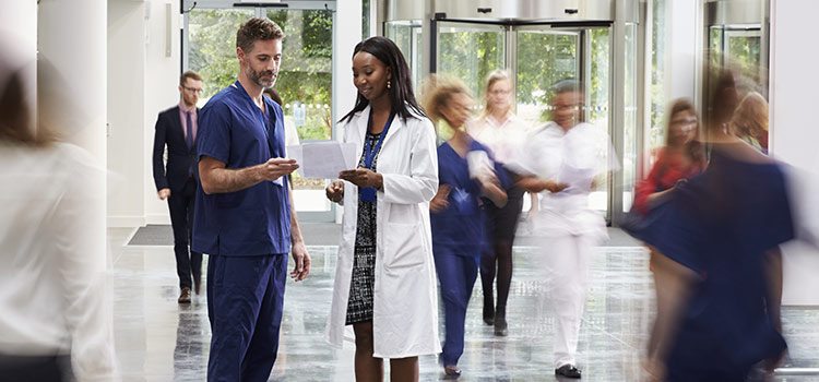 A nurse and physician look at paper documents in a busy hospital foyer