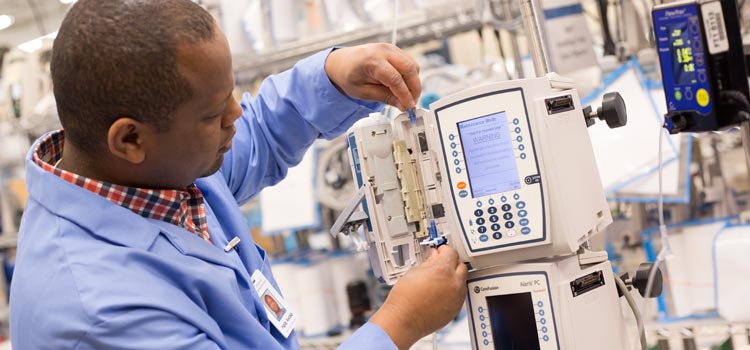 A biomedical technician inserting an IV line into an Alaris LVP during a PM inspection