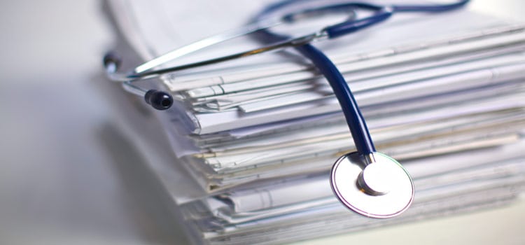 A stethoscope sitting on top of a stack of medical paperwork