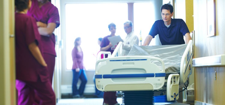 An Agiliti team member pushes a specialty bed down a busy hospital hallway