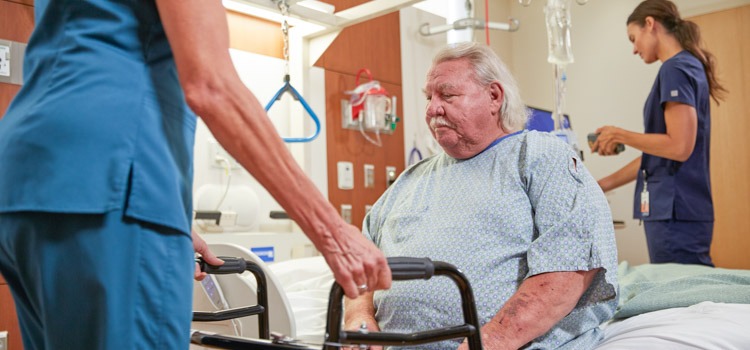 Bariatric patient sitting on edge of specialty hospital bed with a nurse preparing a patient walker