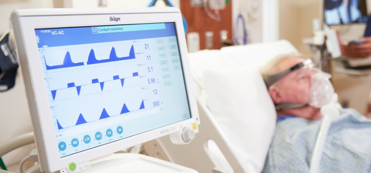 Close up of ventilator with patient in background wearing oxygen mask - infection prevention